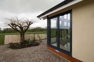 External corner view showing the aluminium Centor bifold doors in matching grey. The doors have are close in spec to the windows with triple glazing and grey aluminium thermally broken frames. 