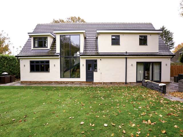 Rear view of property with feature curtain walling area, rear composite door, aluminium bifolds and various casement windows.