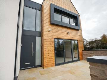 View of entrance featuring RAL7016 grey aluminium door with sandblasted sidelight, bifold doors and aluminium windows.