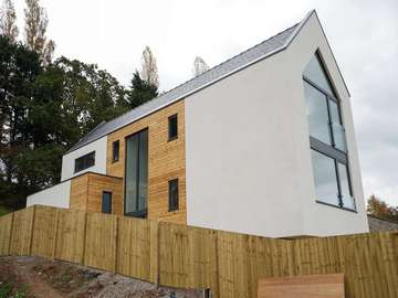 Side view of new build property with timber cladding, k-rend and aluminium curtain walling system.