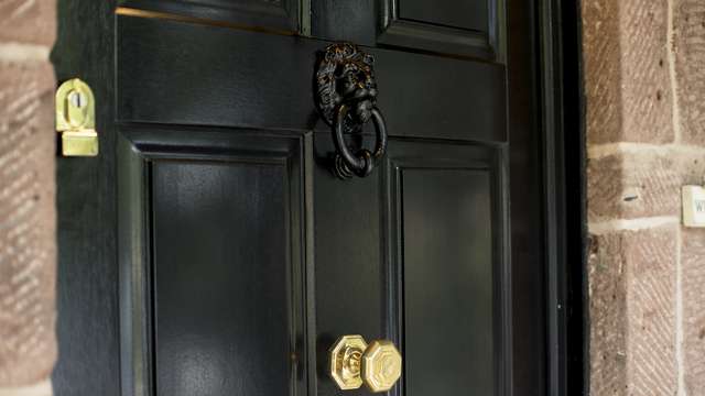 Close up of the brass hardware and black door knocker. Natural timber grain is showing through within the painted finish of the door.