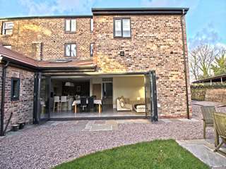 External view of property showing open bi-fold doors and grey uPVC windows.