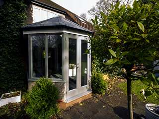 Side shot of conservatory replacement showing Rationel timber aluminium clad windows and doors in green.