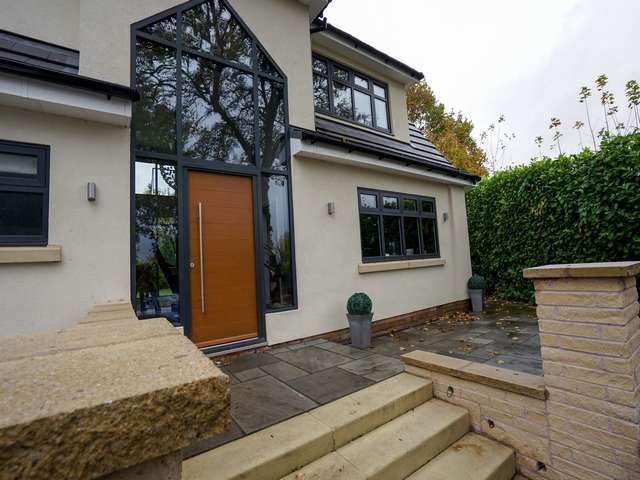 Close up of entrance featuring pitched bespoke aluminium curtain walling system and timber entrance door with brushed stainless steel handle.