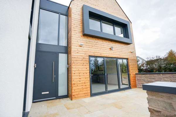 Property entrance full of glazing including contemporary aluminium entrance door with sand-blasted side light, aluminium bifold doors and multiple aluminium windows. Aluminium pressings have been used around some of the windows to give the illusion of a frame that blends seamlessly with the property. All products supplied in RAL 7016 to create a consistent look.
